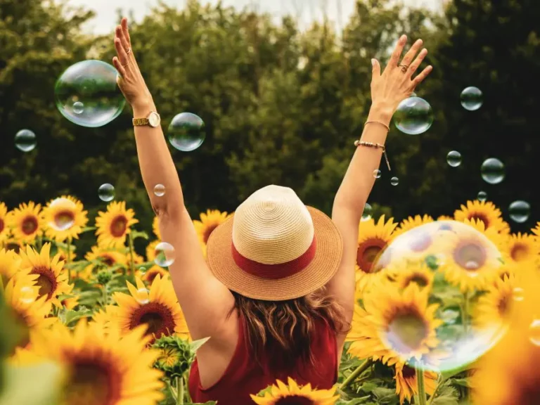 Frau steht in einem Feld aus Sonnenblumen und wirft die Arme überschwänglich in die Luft | Stimmungsbild Hilfe bei Manie Linz